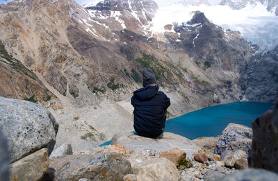 Rear view of man sitting on rock by mountains