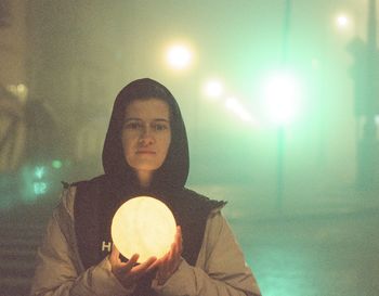 Portrait of young woman standing against sky at night