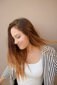 Beautiful woman looking down while standing against brown wall