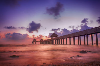 Low angle view of pier over sea against sky during sunset