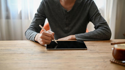 Midsection of man using digital tablet on table