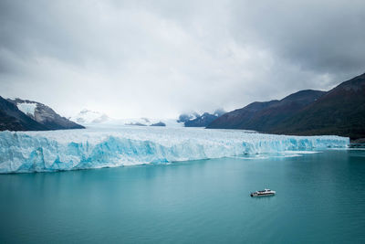 Lake and glacier against snowcapped mountains and cloudy sky