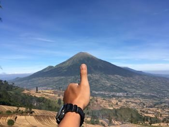 Cropped hand showing thumbs up sign against mountain