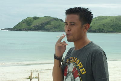 Young man drinking water against sea