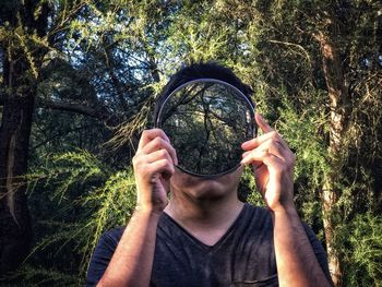 Portrait of young man holding mirror in forest.