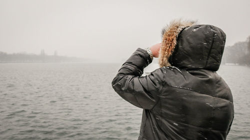 Rear view of man standing by sea against clear sky