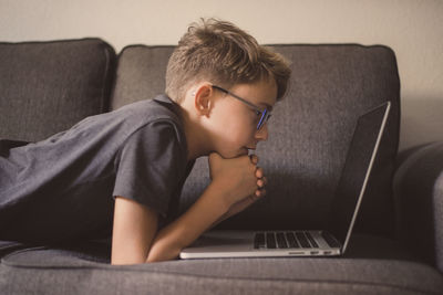Side view of boy using laptop while relaxing on sofa at home
