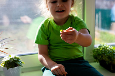 Midsection of boy holding leaf sitting by window