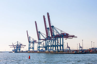 Cranes at commercial dock against clear sky