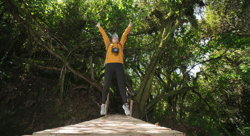 Woman jumping on a wooden bridge, with her arms open, in the middle of a forest