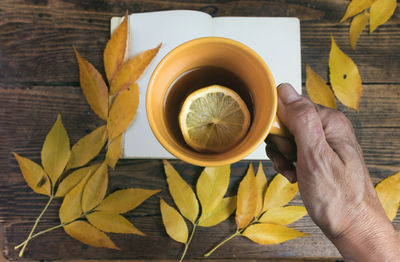 Midsection of woman holding tea cup and yellow leaves