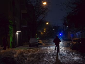 Rear view of man walking on illuminated street at night