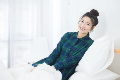 Portrait of smiling young woman sitting on bed at home