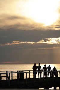 Silhouette people standing on beach against sky during sunset