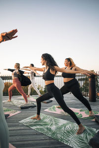 Female friends practicing warrior 2 pose on patio at sunset