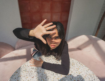 High angle portrait of young woman shielding eyes while sitting at table