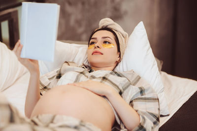 Young pregnant woman reading book at home