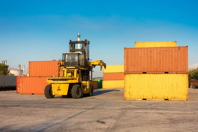 Machinery amidst cargo containers at dock against clear blue sky