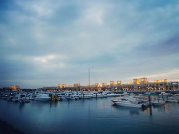 Boats in harbor against cloudy sky
