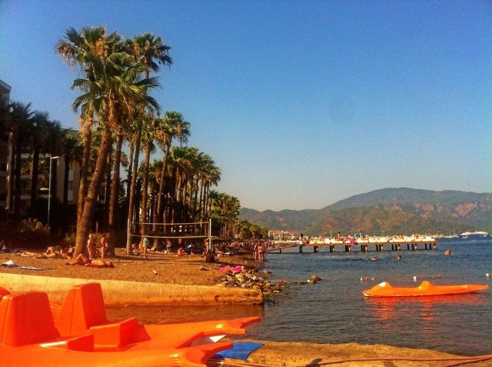 water, clear sky, beach, tree, sea, scenics, blue, sand, shore, tranquil scene, vacations, tranquility, beauty in nature, copy space, nature, large group of people, leisure activity, palm tree, mountain