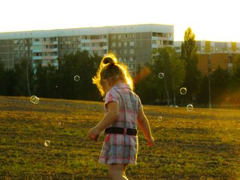 Girl playing with bubbles on field in city