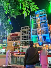 Rear view of man standing on illuminated street in city at night