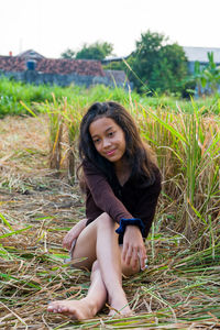 Portrait of smiling young woman sitting on field, looking at camera. 
