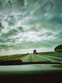 Road against cloudy sky seen through car windshield