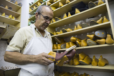 Shoemaker selecting shoe lasts from a shelf in his workshop