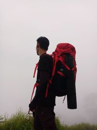 Side view of young man standing on field against sky