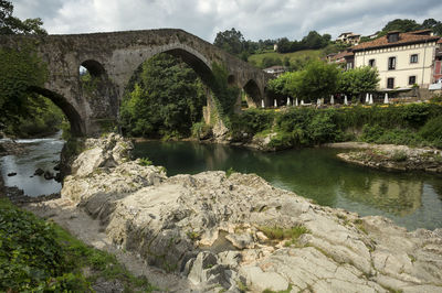 Arch bridge over river by buildings against sky