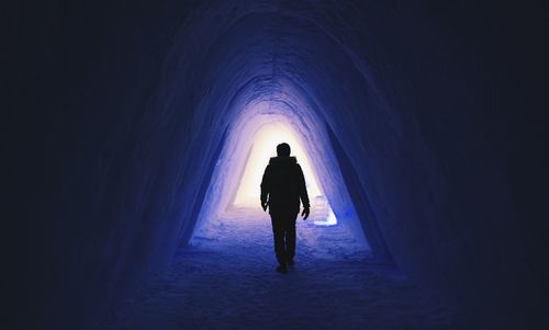 Rear view of silhouette man walking in illuminated tunnel