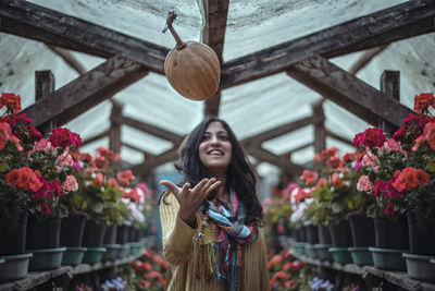 Portrait of smiling young woman standing by flowering plants