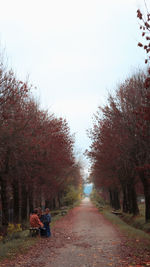 Rear view of people on footpath amidst trees during autumn