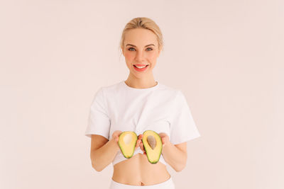 Smiling healthy young woman holds vegetables fruits green avocado on a white isolated background