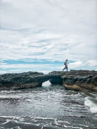 Side view of man on rock by sea against sky