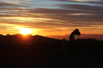 Silhouette man standing on landscape against sky during sunset