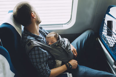 Father on the train holding his sleeping baby in a baby carrier