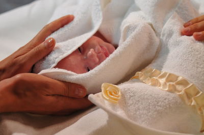 Cropped hands holding baby girl wrapped in towel