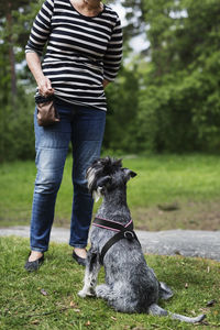 Low section of senior woman standing by dog sitting on field