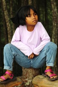 Rear view of woman sitting on rock in forest