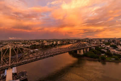 Bridge over river amidst buildings against sky during sunset