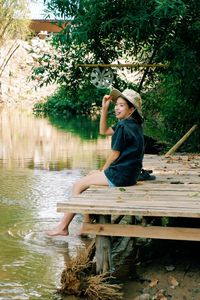 Full length of boy sitting by lake against trees