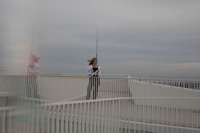 Woman standing on railing against sky