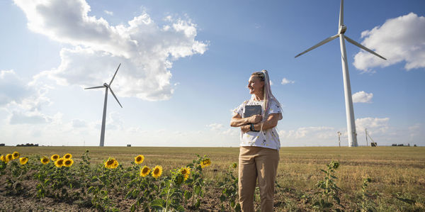 Young smiling woman with tablet in field with sunflowers, wind turbines for green energy produce,eco