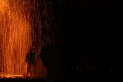 Silhouette person standing by illuminated lights at night