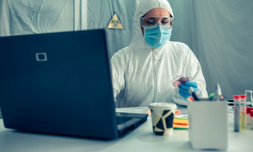 Scientist holding petri dish using laptop on desk