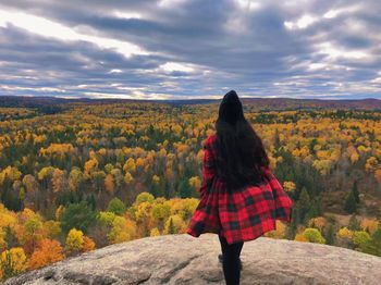 Rear view of woman standing on rock against sky