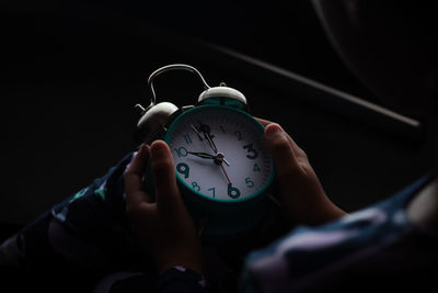 Close-up of hand holding clock against blurred background