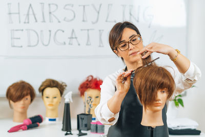 Hairdresser educator with students, explaining hair cutting technique on mannequin head for training